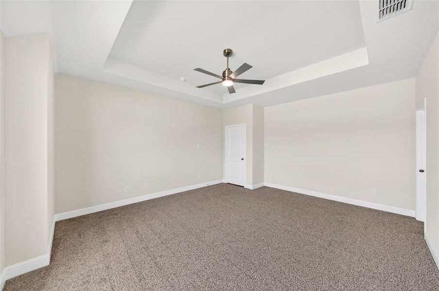 Carpeted room featuring a tray ceiling with a ceiling fan, white baseboards, and neutral wall tones