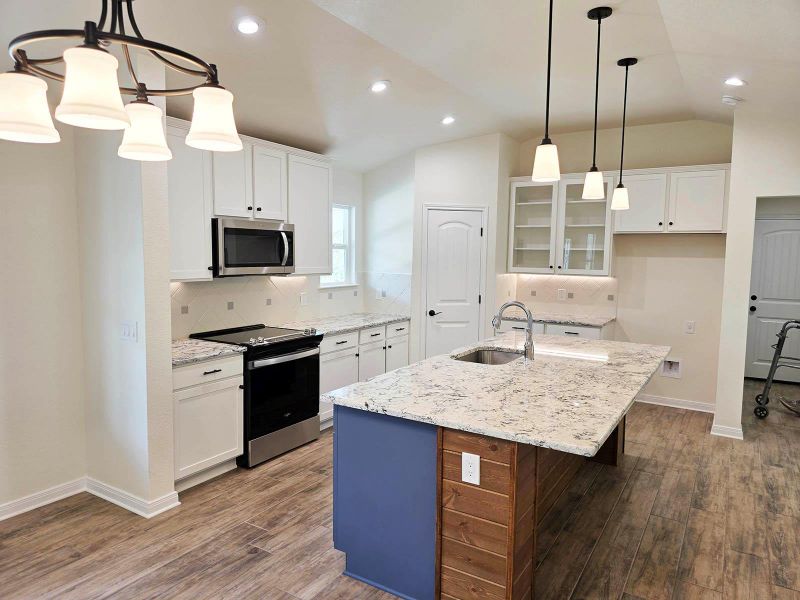 Kitchen featuring white cabinetry, stainless steel appliances, glass insert cabinets, lofted ceiling, and an island with sink
