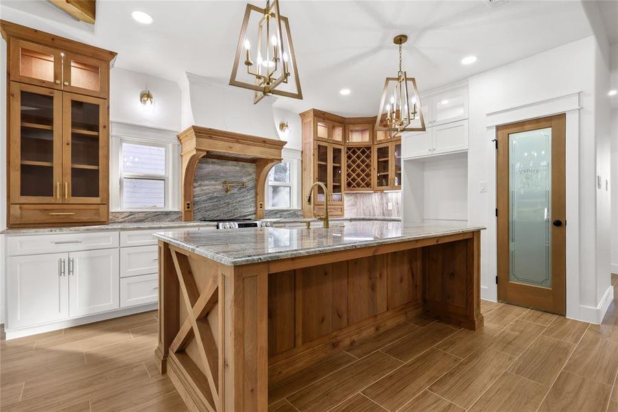Kitchen featuring glass insert cabinets, white cabinets, light stone countertops, wood tiled floors, and recessed lighting
