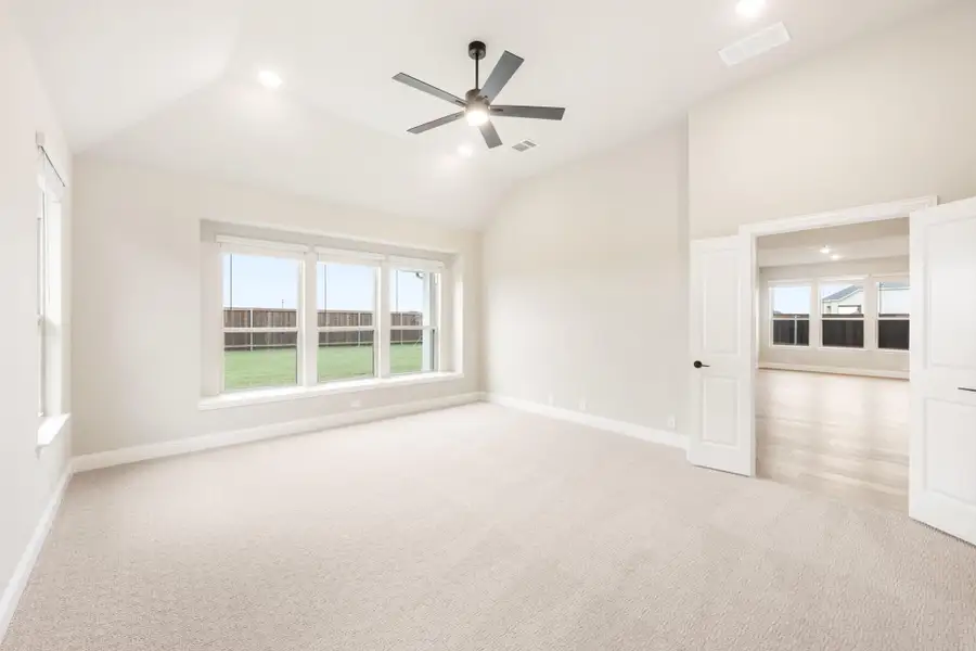 Empty bedroom with vaulted ceiling, ceiling fan, carpet flooring, and large backyard-facing windows