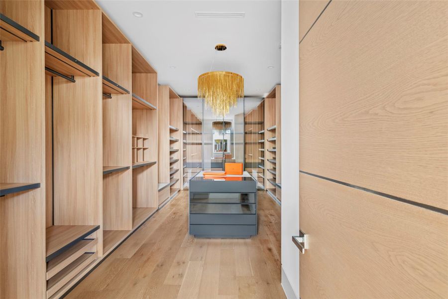 [Primary Closet] Custom-fitted walk-in closet in the primary suite, this closet offers a packing island, clothes racks, and abundant shelving. Avenue Lighting waterfall chandelier.