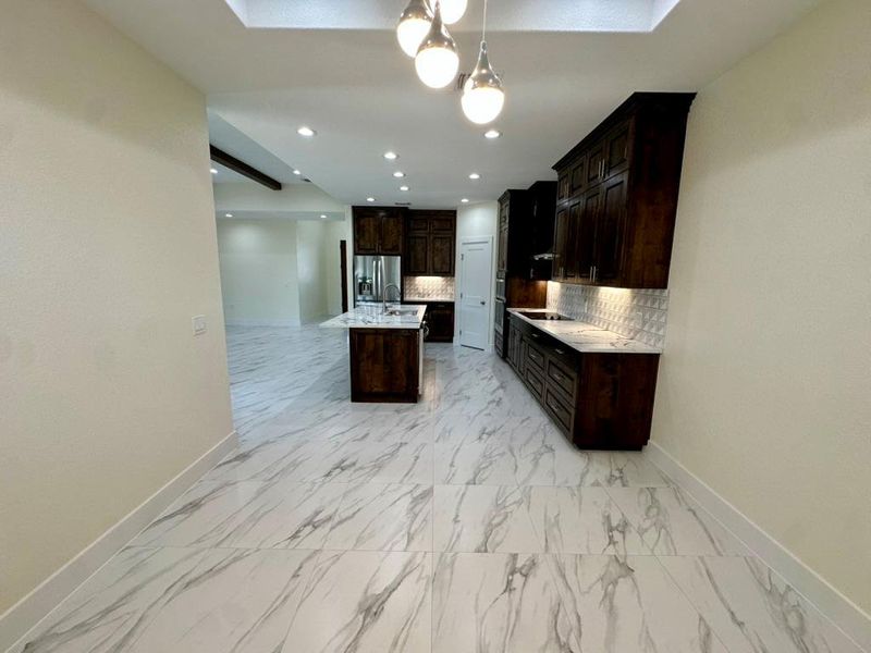 Kitchen featuring a center island with sink, backsplash, dark brown cabinets, open floor plan, and hanging light fixtures