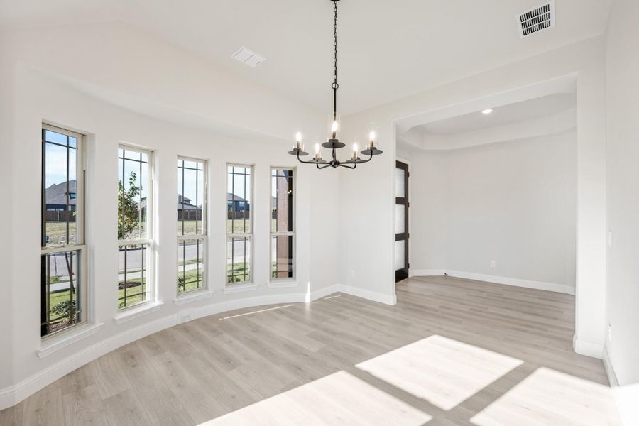 Empty dining room with curved bay windows, black chandelier, and light hardwood floors