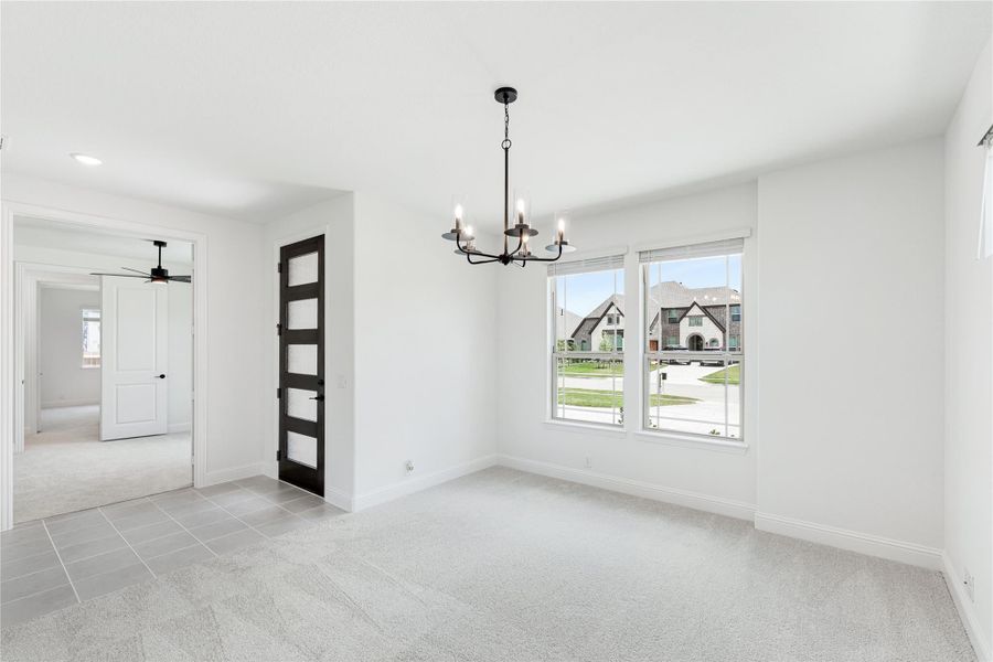 Empty dining room with black chandelier, carpet flooring, and large window overlooking neighborhood