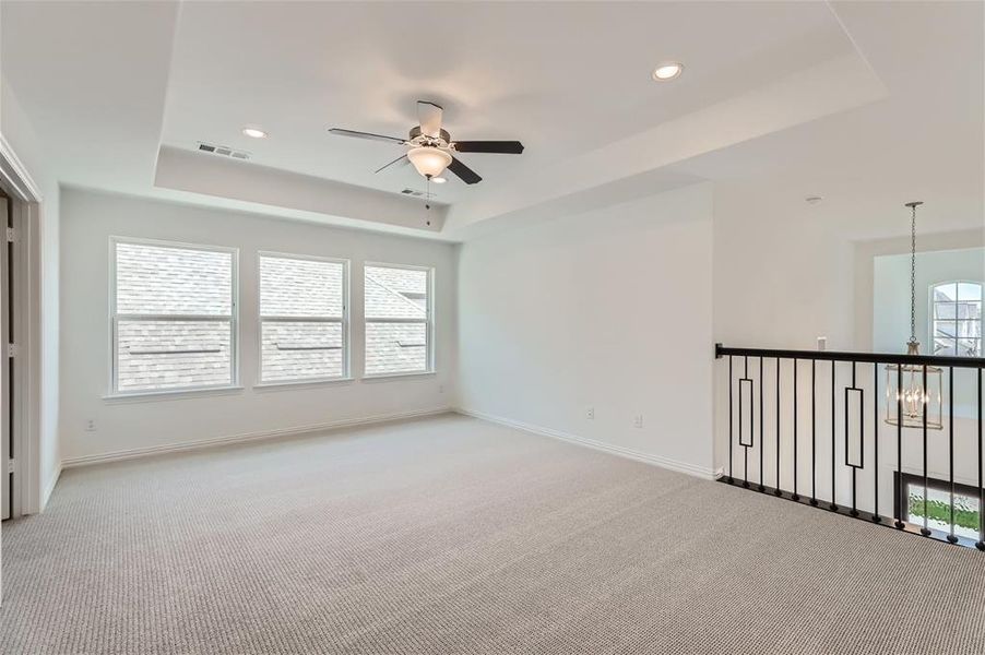 Empty room with a tray ceiling, carpet floors, and ceiling fan with notable chandelier