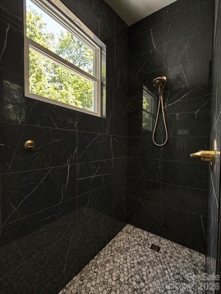 Walk-in shower  features hi-gloss marble look porcelain walls & honeycomb tile floors.
