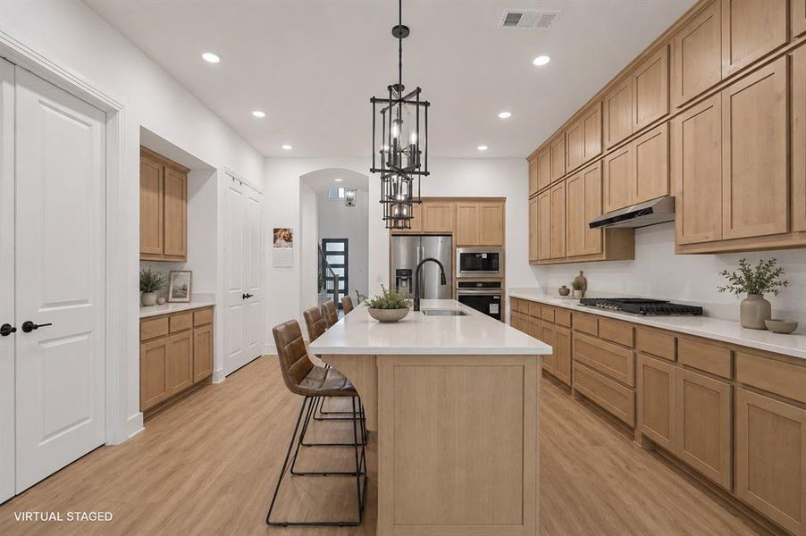 Expansive kitchen featuring wood-finish flooring, a large central island with seating, extensive cabinetry, light countertops, and recessed lighting Expansive kitchen featuring wood-finish flooring, a large central island with seating, extensive cabinetry, light countertops, and recessed lighting
