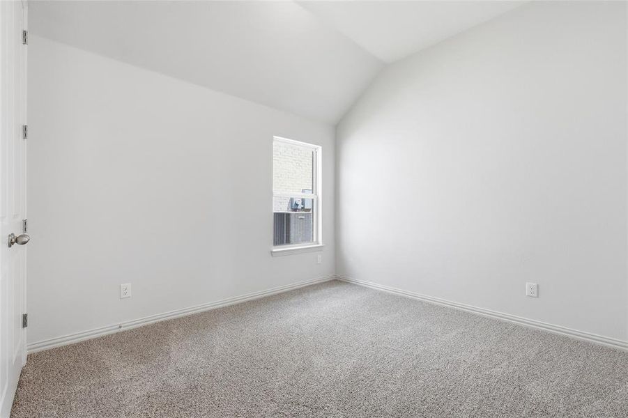Carpeted spare room featuring vaulted ceiling and baseboards