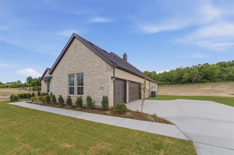 View of property exterior featuring stone siding, driveway, a chimney, an attached garage, and a yard