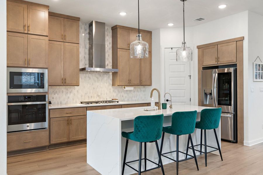 Modern kitchen featuring a white countertop island, stainless steel appliances, light wood-finish cabinetry, a geometric tile backsplash, and recessed lighting