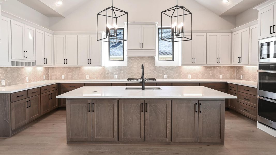 Kitchen featuring an island with sink, decorative backsplash, pendant lighting, white cabinetry, and light wood finished floors Kitchen featuring an island with sink, decorative backsplash, pendant lighting, white cabinetry, and light wood finished floors