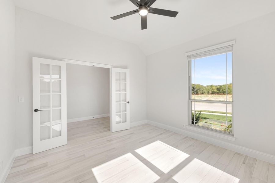 Empty room with light wood floors, ceiling fan, large window, and white French doors