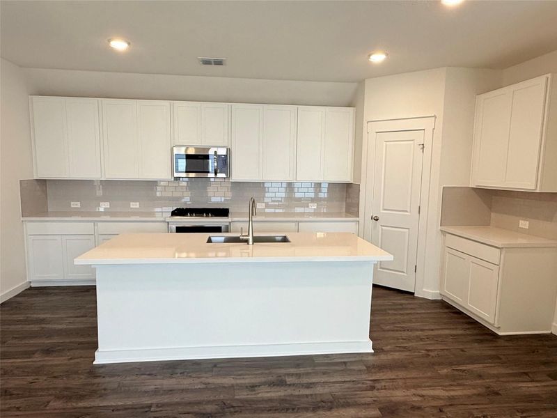 Kitchen with stainless steel microwave, backsplash, a kitchen island with sink, dark wood-type flooring, and recessed lighting Kitchen with stainless steel microwave, backsplash, a kitchen island with sink, dark wood-type flooring, and recessed lighting