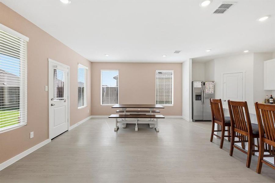 Open-concept living space featuring light-toned flooring, multiple windows with blinds, a white paneled door, and recessed lighting Open-concept living space featuring light-toned flooring, multiple windows with blinds, a white paneled door, and recessed lighting