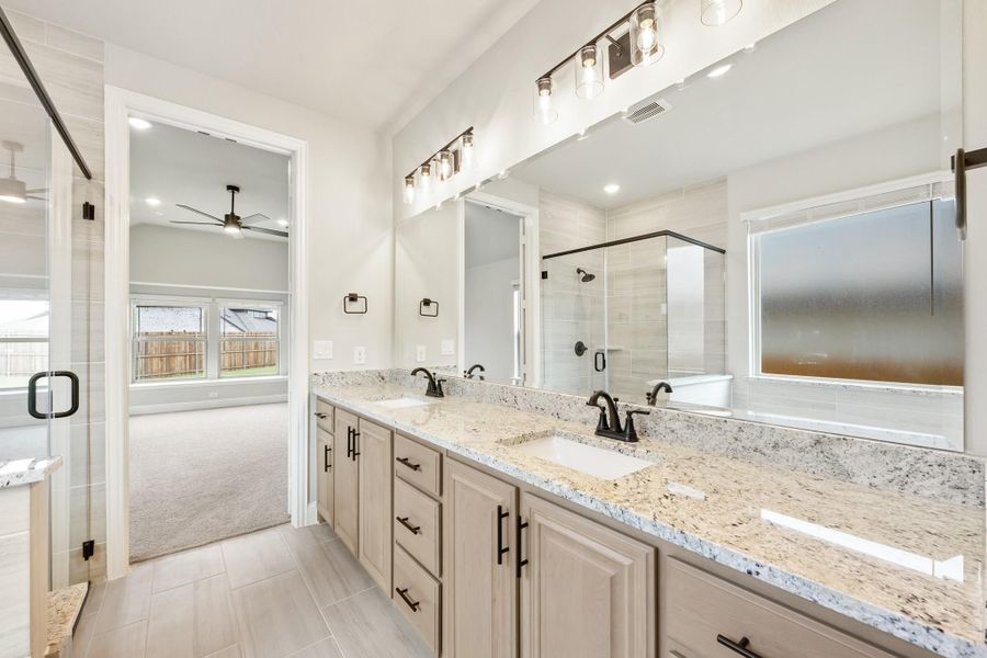 Master bathroom with double vanity, granite countertops, glass shower, and view into carpeted bedroom Master bathroom with double vanity, granite countertops, glass shower, and view into carpeted bedroom