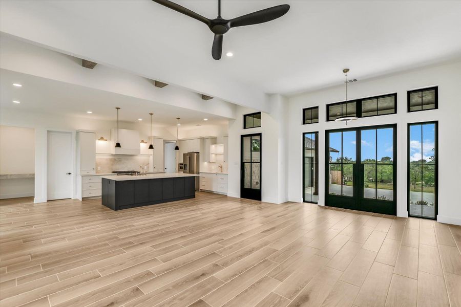 Spacious interior with light wood-finish flooring, featuring a kitchen with a dark-toned island, white cabinetry, and stainless steel appliances
