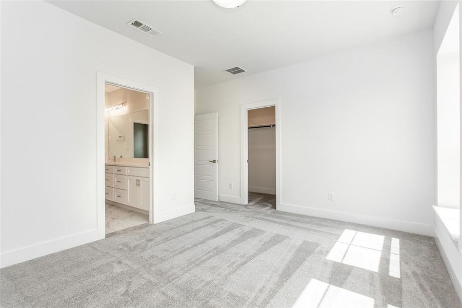 Unfurnished bedroom with a walk in closet, light carpet, a closet, and ensuite bath