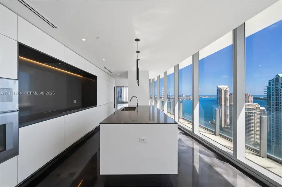 Sleek kitchen featuring floor-to-ceiling windows, high-gloss cabinetry, a central island with integrated sink, and recessed lighting Sleek kitchen featuring floor-to-ceiling windows, high-gloss cabinetry, a central island with integrated sink, and recessed lighting