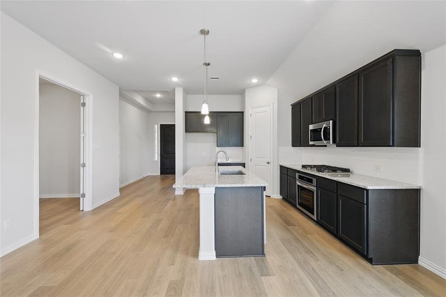 Kitchen featuring a sink, stainless steel appliances, light stone countertops, light wood-style floors, and pendant lighting