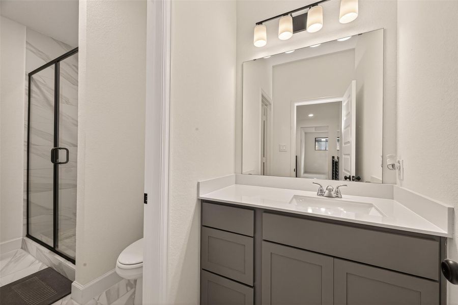This modern bathroom features a sleek vanity with a large mirror, contemporary lighting, and a glass-enclosed shower. The neutral tones create a clean and inviting space.