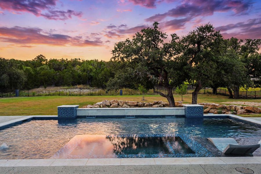 A sparkling geometric pool is framed by mature trees and a scenic natural backdrop.