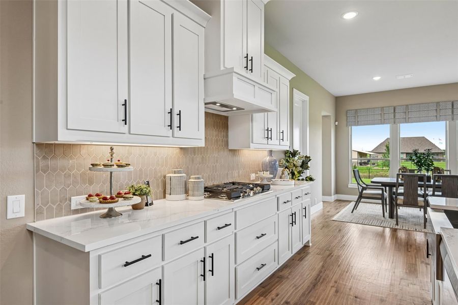 Kitchen with white cabinets, quartz countertops, tile backsplash, and hardwood floors open to dining area Kitchen with white cabinets, quartz countertops, tile backsplash, and hardwood floors open to dining area