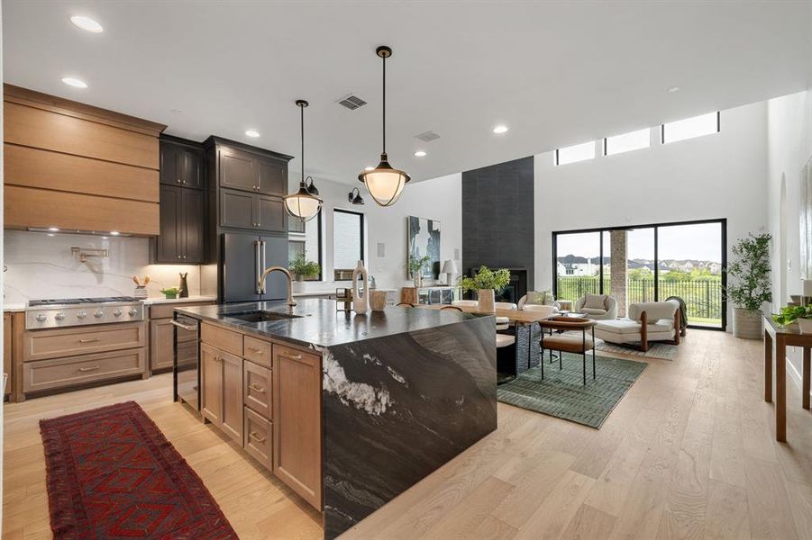 Kitchen with light wood-style floors, dark stone counters, recessed lighting, appliances with stainless steel finishes, and a center island with sink Kitchen with light wood-style floors, dark stone counters, recessed lighting, appliances with stainless steel finishes, and a center island with sink