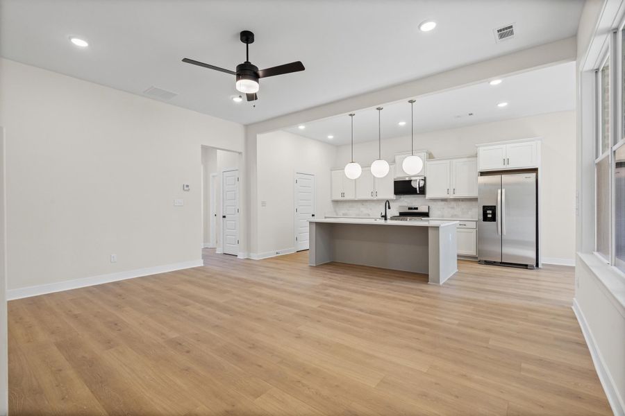 Kitchen featuring stainless steel appliances, open floor plan, white cabinets, pendant lighting, and an island with sink Kitchen featuring stainless steel appliances, open floor plan, white cabinets, pendant lighting, and an island with sink