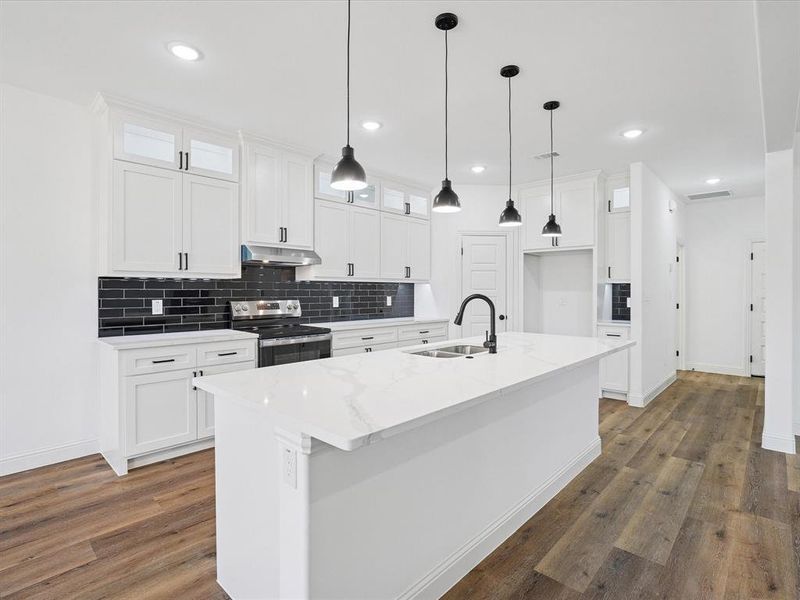 Kitchen featuring white cabinetry, stainless steel electric range, light stone countertops, a center island with sink, and glass fronted cabinets