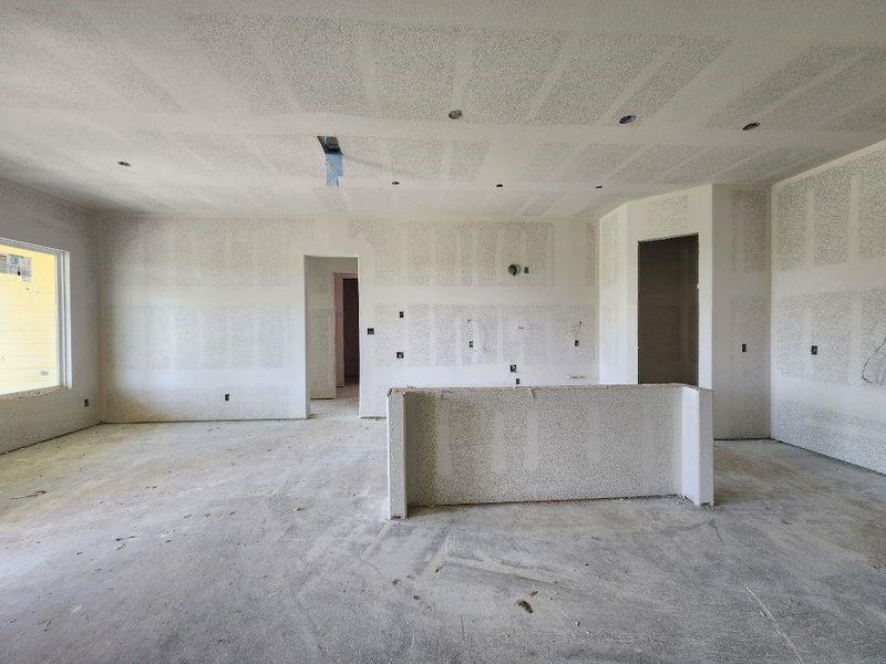 Open concept living space featuring a partial-height wall, multiple electrical outlets, recessed lighting provisions, a large window opening, and a doorway