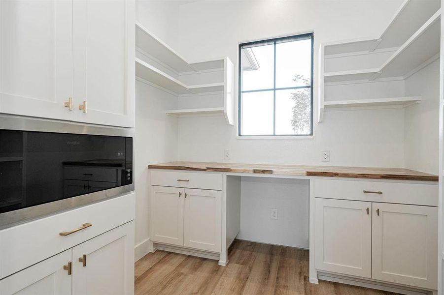 Example of builders pantry w butcher block countertops, stainless steel microwave, light wood-type flooring