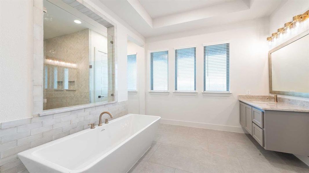 Bathroom with tile patterned flooring, vanity, a tub to relax in, and a tray ceiling