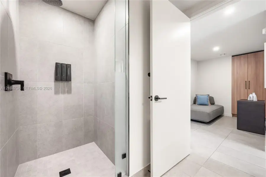 Walk-in shower featuring matte black fixtures, rainfall showerhead, and floor-to-ceiling large-format tile, complemented by a glass panel enclosure and light-toned tile flooring Walk-in shower featuring matte black fixtures, rainfall showerhead, and floor-to-ceiling large-format tile, complemented by a glass panel enclosure and light-toned tile flooring