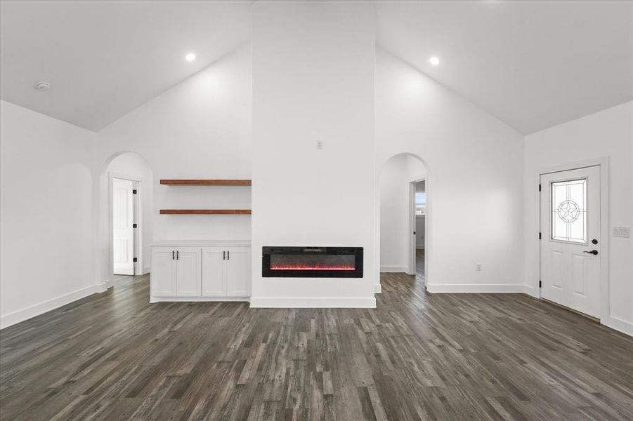 Unfurnished living room featuring high vaulted ceiling and dark hardwood / wood-style floors