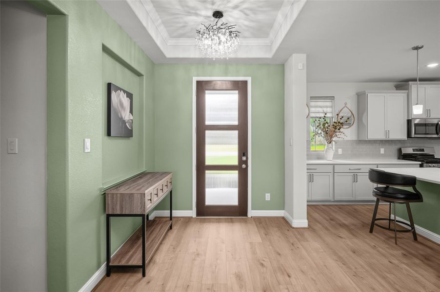 Welcoming foyer with tray ceiling and modern chandelier.