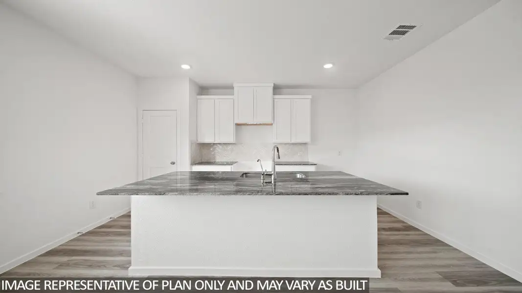 Kitchen featuring an expansive island with a stone countertop and integrated sink, white shaker-style cabinetry, stainless steel faucet, and recessed lighting
