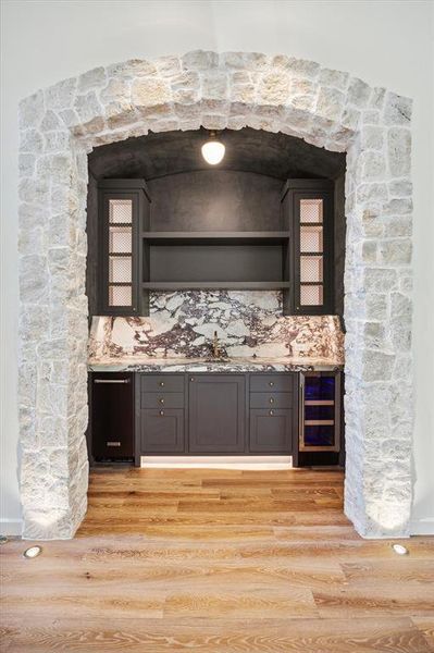 Wet bar complete with separate ice maker, beverage cooler, sink, marble counters under a stone archway and lime wash paint matched to the cabinets, this area is perfect for entertaining and hosting