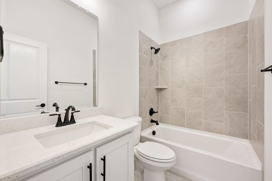 Full bathroom with white vanity, quartz countertop, tub-shower combo with beige tile, and black fixtures