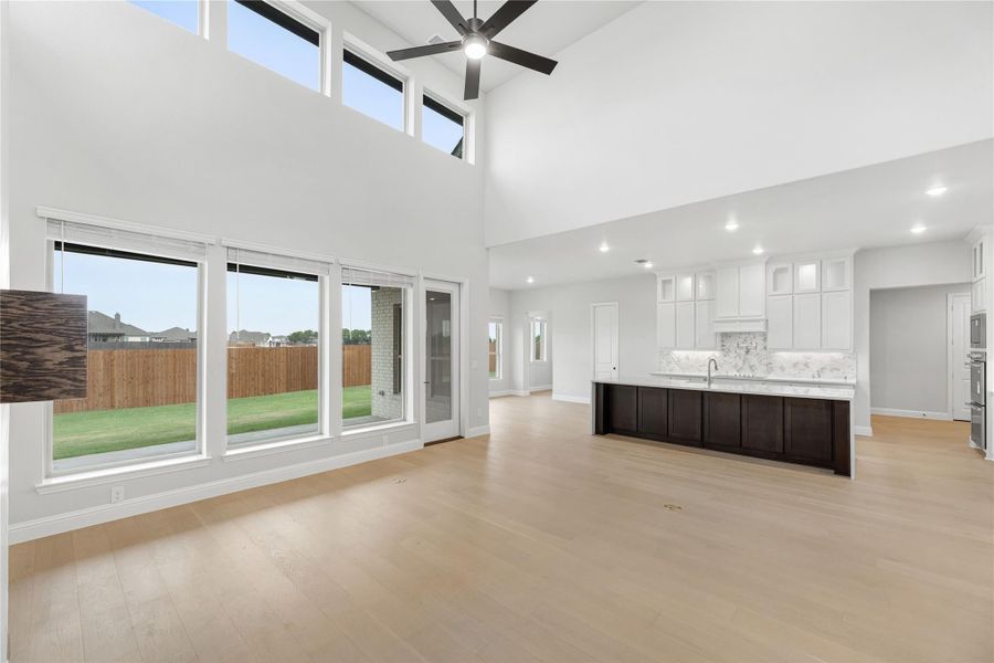 Open living area with two-story ceiling, ceiling fan, hardwood floors, and open kitchen with dark island and white cabinets