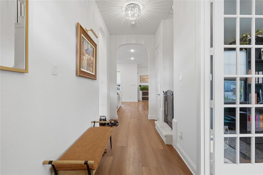 Hallway featuring wood-finish flooring, crisp white walls, and a recessed archway Hallway featuring wood-finish flooring, crisp white walls, and a recessed archway