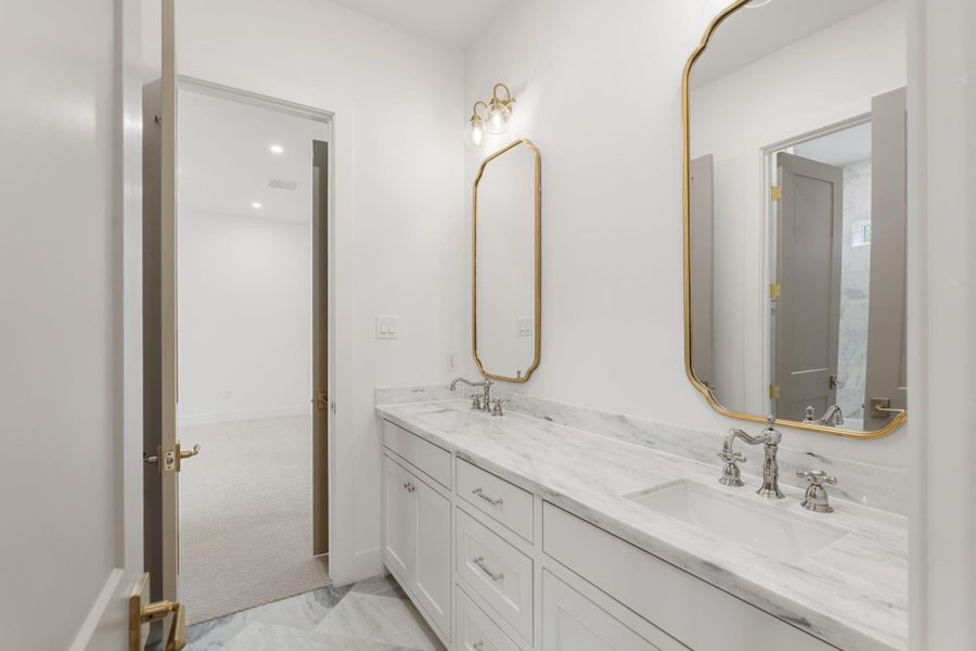 Attached full bath featuring a marble countertop vanity with ample drawer storage and upgraded fixtures. The walk-in glass shower showcases full-height tile and a detailed tile floor for added texture and interest. Brass sconces and a framed mirror provide a refined finish, creating a bright and well-appointed private bath for guests.