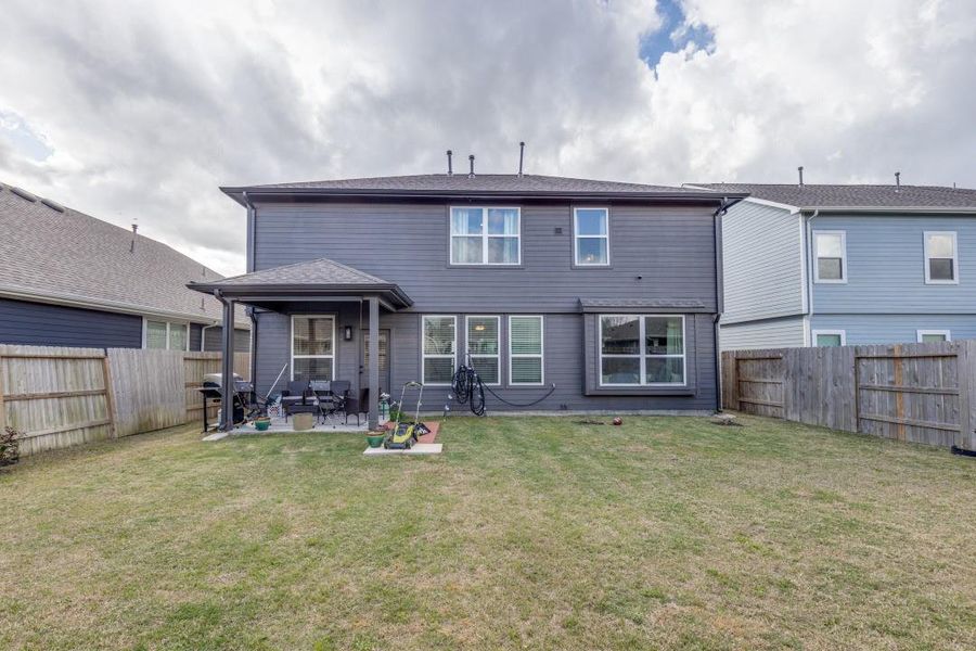 This is a two-story home with a spacious backyard, featuring a covered patio area. The exterior is a modern gray, with large windows for natural light. The property is enclosed by a wooden fence, offering privacy. Perfect for outdoor entertaining or family activities.