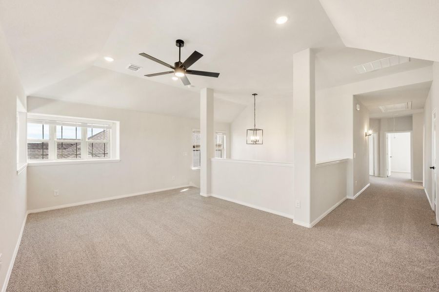 Open living area with vaulted ceiling, ceiling fan, carpet flooring, and hallway leading to other rooms
