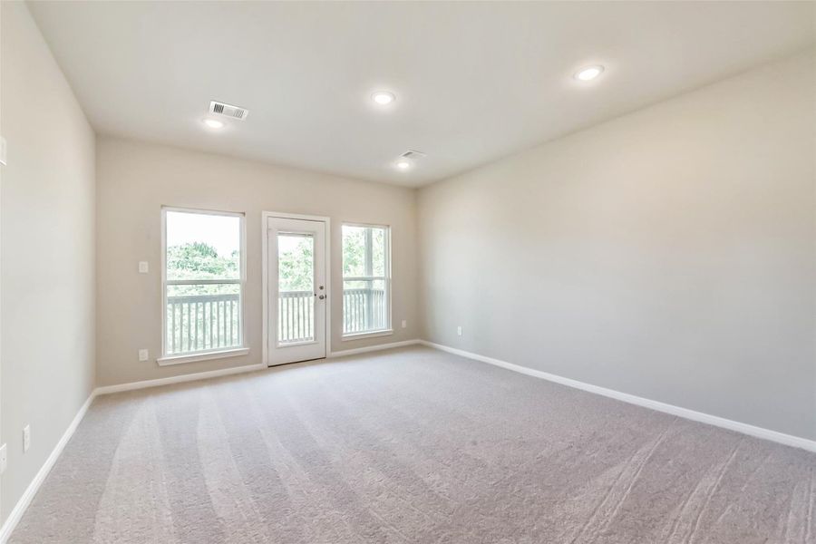 The primary bedroom is spacious, bright, and airy, featuring carpeted flooring and a door that opens to the balcony.
