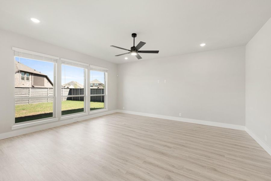 Empty living room with light wood floors, ceiling fan, and large windows overlooking backyard