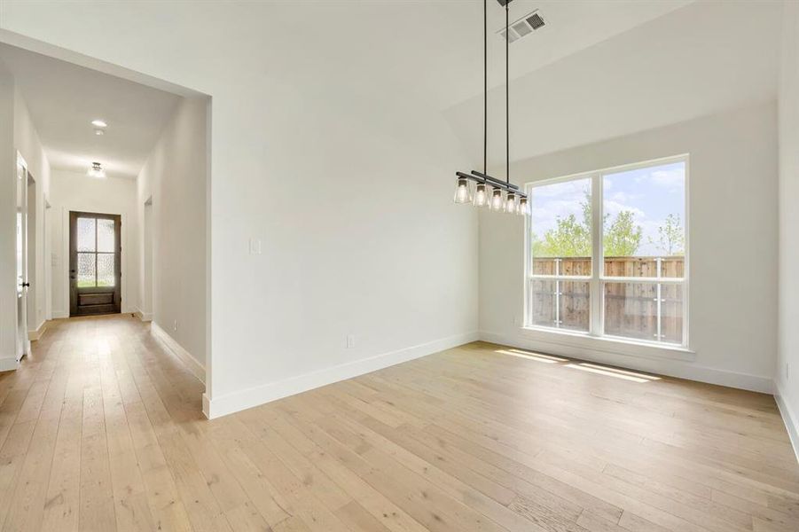 Spacious room featuring wood-finish flooring, a contemporary linear chandelier, and a large window Spacious room featuring wood-finish flooring, a contemporary linear chandelier, and a large window