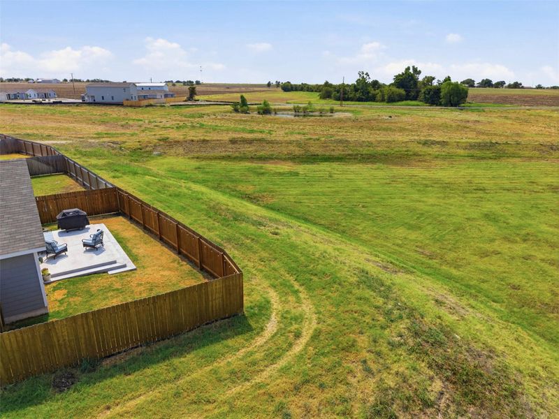 Rolling green hills stretch beyond a fenced yard, creating a peaceful and serene backdrop.