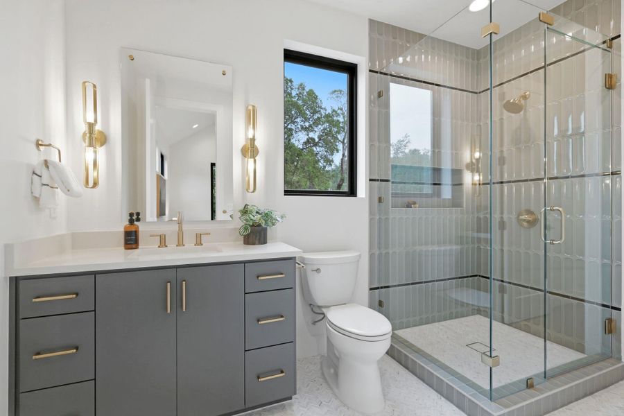 Bathroom featuring a gray vanity with gold-finish hardware, a walk-in shower with glass enclosure, vertical subway tile, and two windows