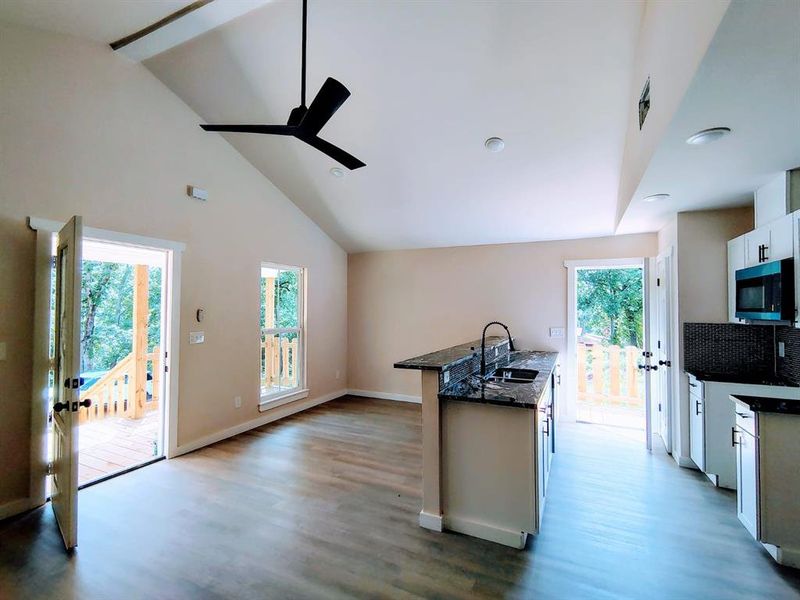 Kitchen with stainless steel microwave, a ceiling fan, wood finished floors, white cabinetry, and high vaulted ceiling