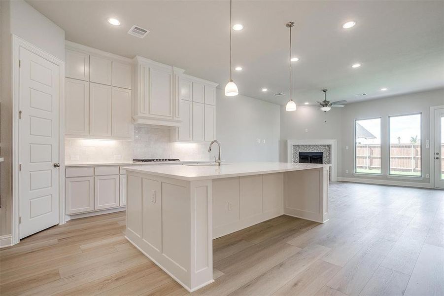 Kitchen with white cabinets, tasteful backsplash, a kitchen island with sink, and light wood-type flooring